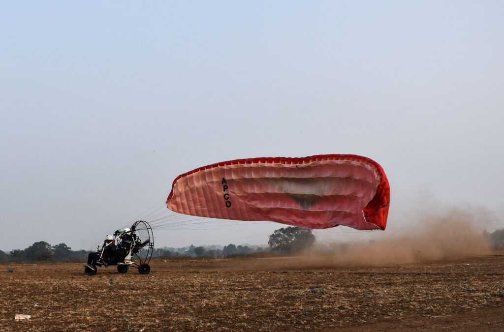 Exciting paramotoring activity in Ahmednagar, with a vibrant red parachute against a clear sky.